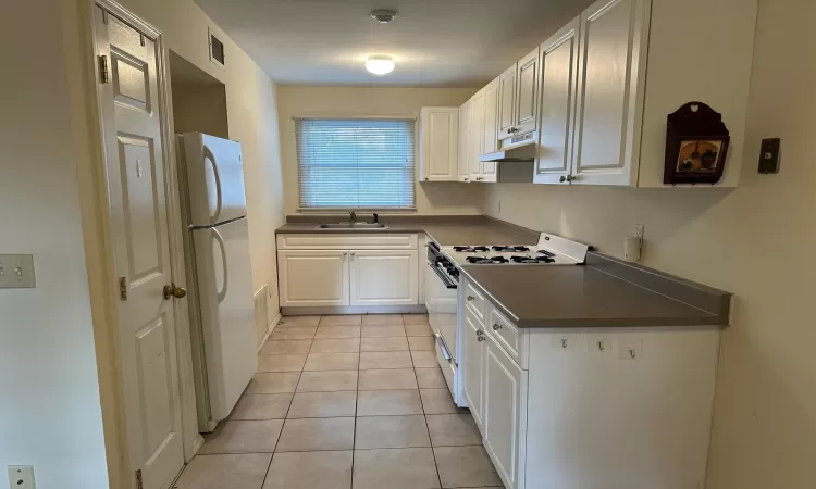 Kitchen with white cabinetry, light tile patterned flooring, white appliances, and sink