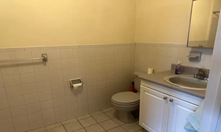 Bathroom with toilet, vanity, tile patterned floors, and tile walls