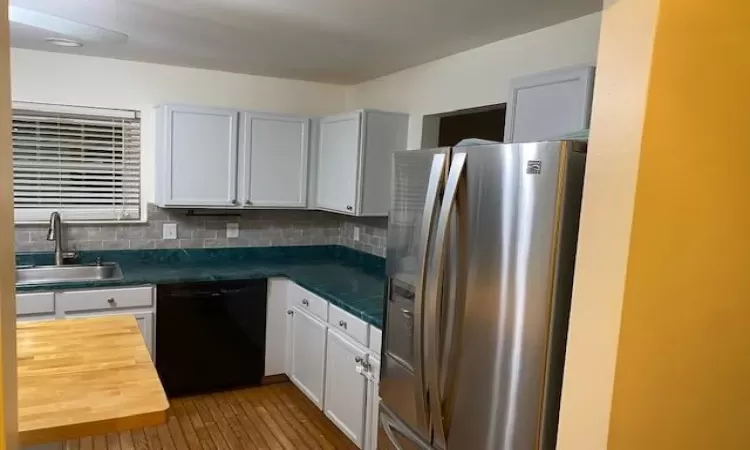 Kitchen featuring dishwasher, backsplash, white cabinets, sink, and stainless steel refrigerator with ice dispenser