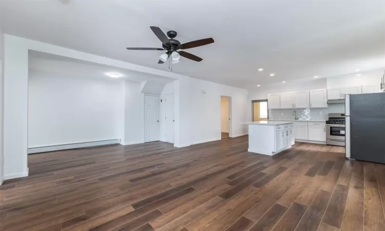 Kitchen with white cabinets, appliances with stainless steel finishes, a baseboard radiator, a kitchen island, and dark hardwood / wood-style flooring