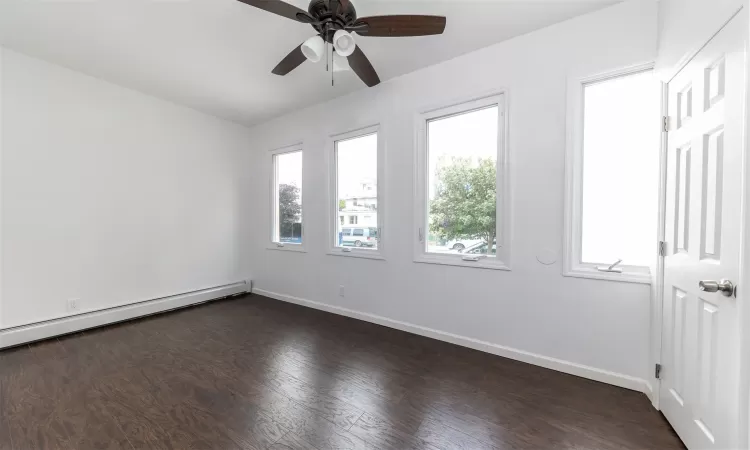 Unfurnished room with baseboard heating, ceiling fan, and dark hardwood / wood-style floors