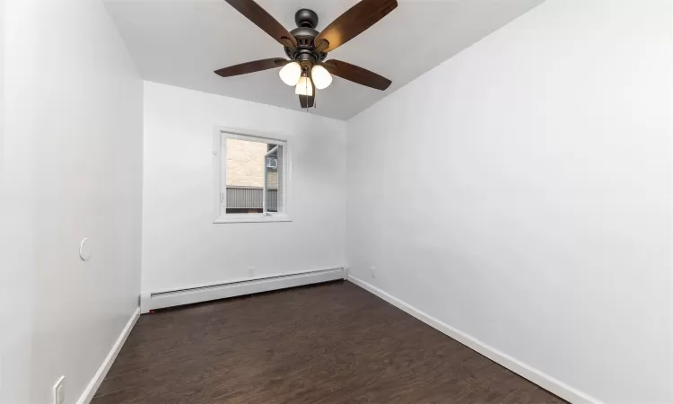 Empty room with ceiling fan, dark wood-type flooring, and a baseboard heating unit