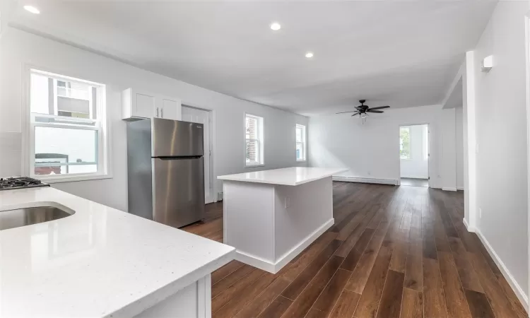 Kitchen with ceiling fan, dark hardwood / wood-style floors, a kitchen island, white cabinetry, and stainless steel refrigerator