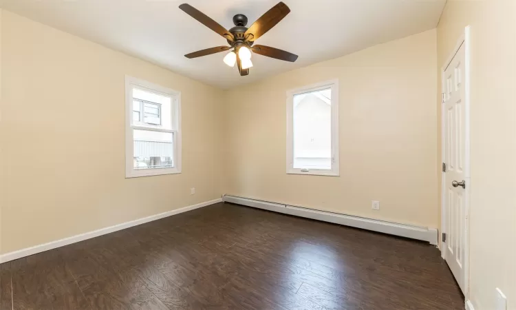 Empty room with ceiling fan, dark hardwood / wood-style flooring, and a baseboard radiator