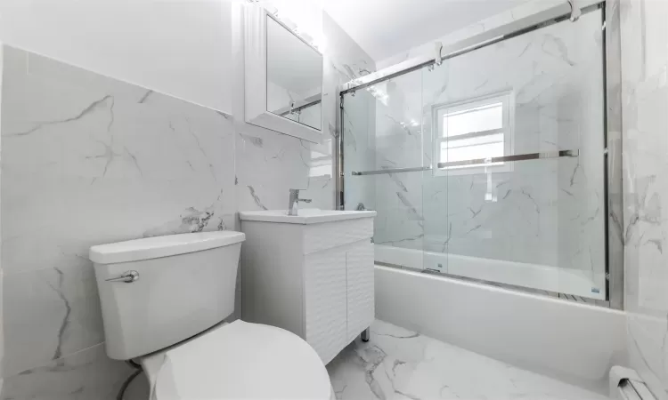 Full bathroom with vanity, a baseboard heating unit, combined bath / shower with glass door, toilet, and tile walls