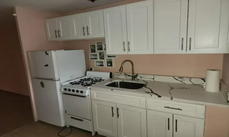 Kitchen with white appliances, white cabinetry, and sink