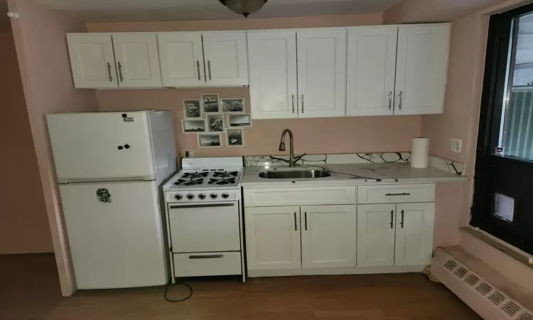 Kitchen with white cabinetry, sink, a baseboard heating unit, white appliances, and hardwood / wood-style flooring