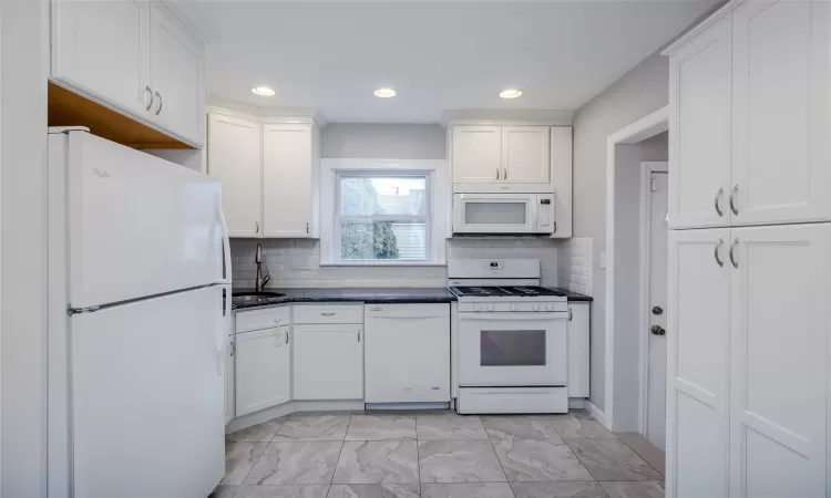 Kitchen featuring decorative backsplash, white appliances, white cabinetry, and sink