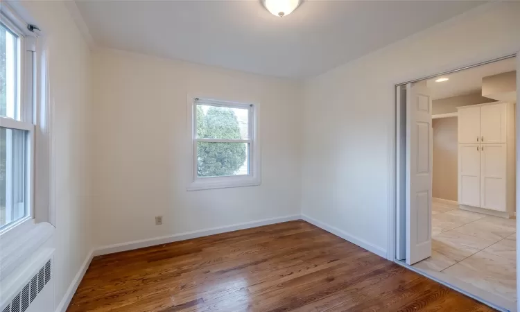 Empty room with crown molding, radiator heating unit, and hardwood / wood-style flooring