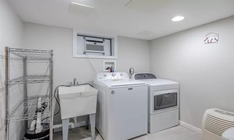 Clothes washing area with light tile patterned floors, sink, a wall mounted AC, and washing machine and clothes dryer