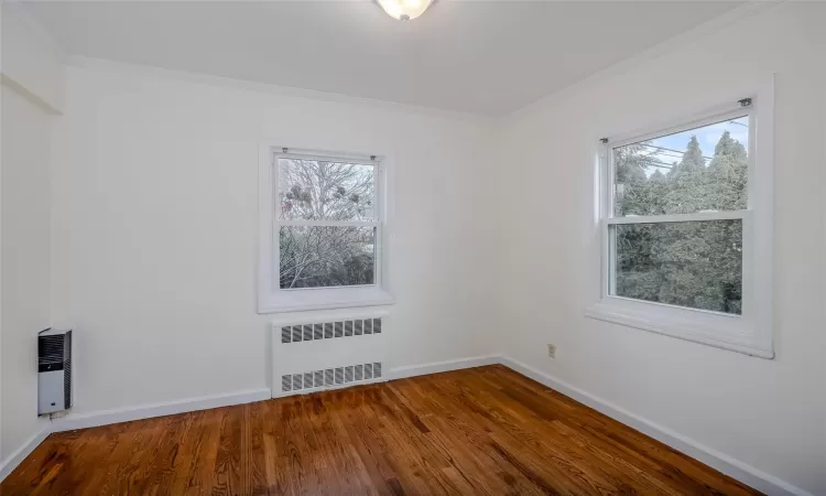 Empty room with wood-type flooring, heating unit, radiator, and crown molding