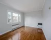 Empty room with wood-type flooring, radiator heating unit, crown molding, and heating unit