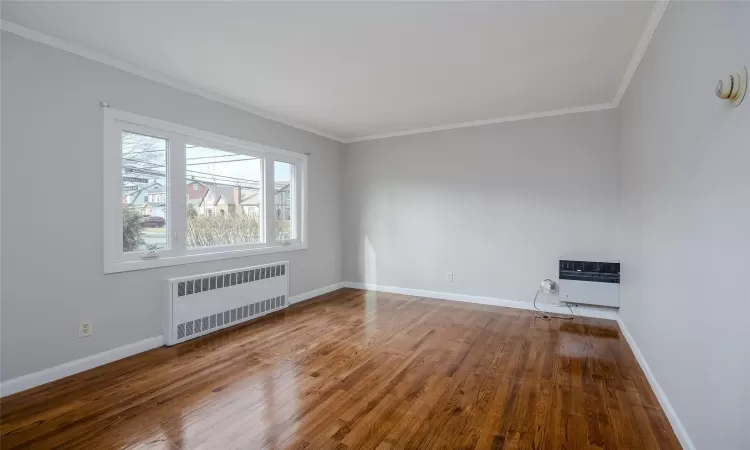 Empty room with wood-type flooring, radiator heating unit, crown molding, and heating unit