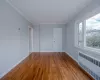 Empty room with hardwood / wood-style floors, radiator heating unit, and ornamental molding