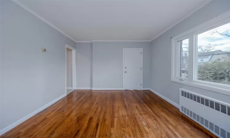 Empty room with hardwood / wood-style floors, radiator heating unit, and ornamental molding