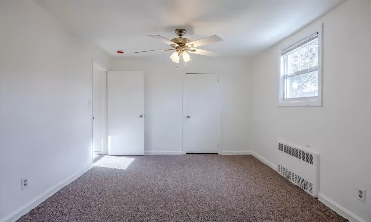 Unfurnished bedroom with carpet, radiator heating unit, and ceiling fan