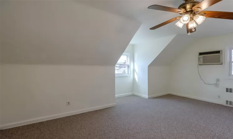 Additional living space with vaulted ceiling, carpet flooring, ceiling fan, a wall mounted AC, and radiator heating unit