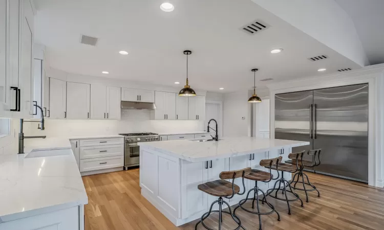 Kitchen featuring white cabinetry, dishwasher, an island with sink, decorative light fixtures, and vaulted ceiling