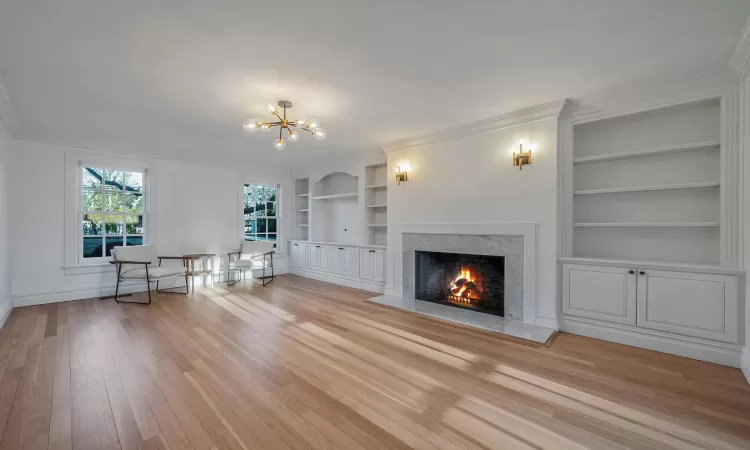 Unfurnished living room featuring a high end fireplace, an inviting chandelier, crown molding, light wood-type flooring, and built in features