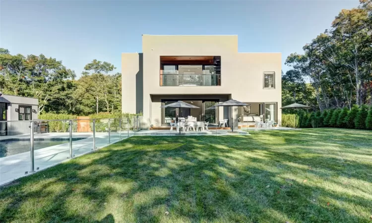 Back of house with a fenced in pool, a patio area, a balcony, and a yard