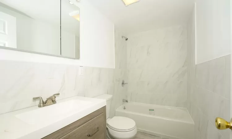 Full bathroom with vanity, toilet, tile walls, and tiled shower / bath