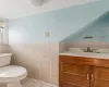 Bathroom featuring tile patterned floors, vaulted ceiling, toilet, vanity, and tile walls