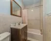 Full bathroom with vanity, shower / bathtub combination with curtain, tile walls, and toilet