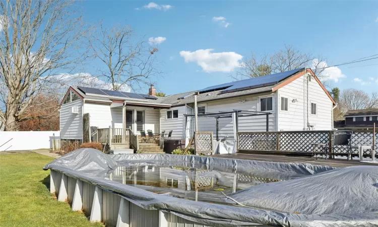 Back of house featuring a swimming pool side deck, solar panels, and a yard