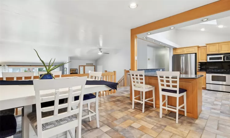 Kitchen featuring decorative backsplash, dark stone counters, stainless steel appliances, a center island, and lofted ceiling