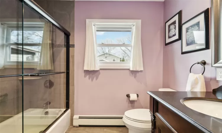 Full bathroom featuring vanity, a baseboard heating unit, bath / shower combo with glass door, tile patterned flooring, and toilet