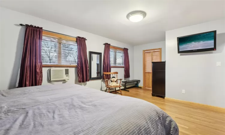 Bedroom featuring hardwood / wood-style flooring, a baseboard radiator, and a wall unit AC