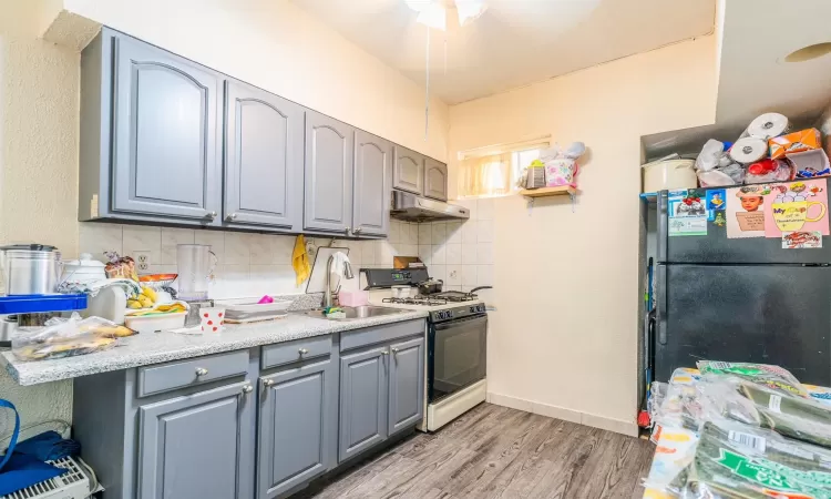 Kitchen featuring decorative backsplash, white range with gas cooktop, sink, light hardwood / wood-style floors, and stainless steel refrigerator