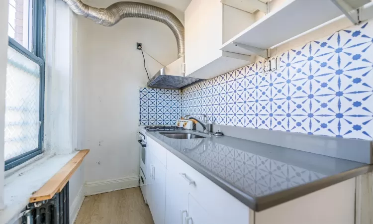 Kitchen featuring light wood-type flooring, tasteful backsplash, sink, white cabinets, and butcher block countertops