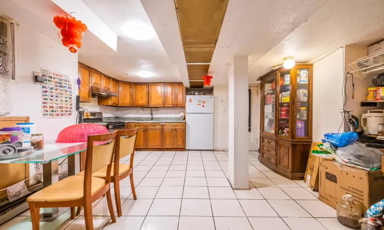 Kitchen with white refrigerator, light tile patterned floors, a textured ceiling, and gas range