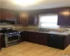 Kitchen featuring gas stove, dark brown cabinetry, sink, light tile patterned floors, and black dishwasher