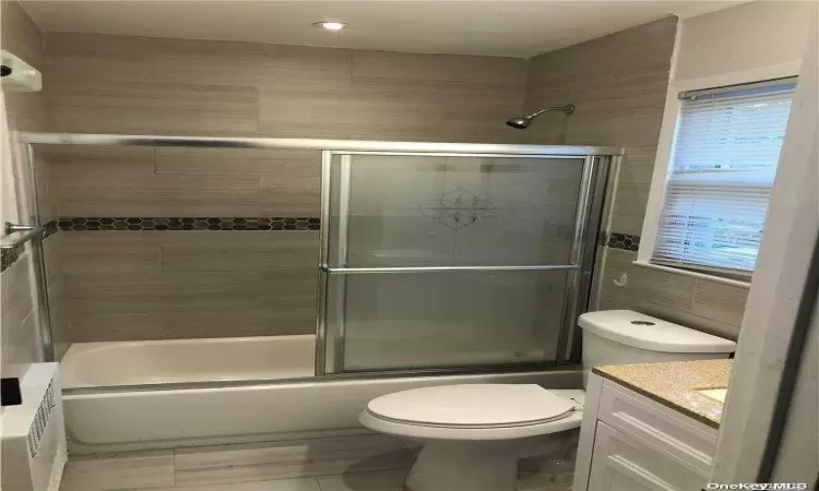 Full bathroom featuring vanity, toilet, tile walls, and combined bath / shower with glass door