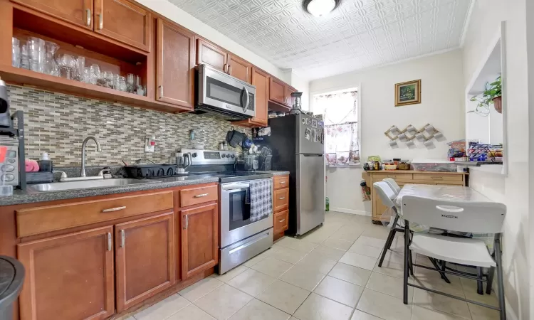 Kitchen featuring crown molding, sink, decorative backsplash, appliances with stainless steel finishes, and light tile patterned flooring