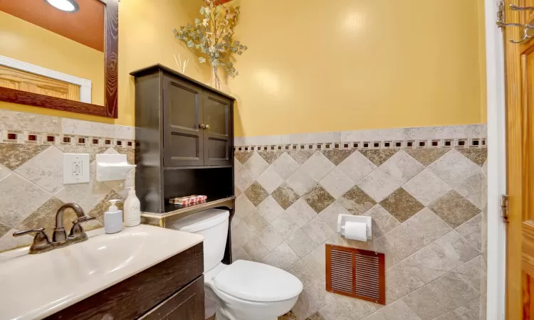 Bathroom featuring vanity, toilet, and tile walls