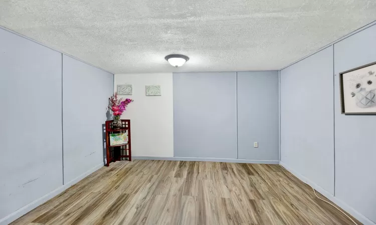 Empty room with a textured ceiling and light hardwood / wood-style flooring