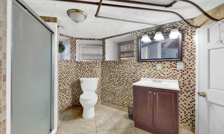 Bathroom with vanity, tile patterned flooring, toilet, a textured ceiling, and a shower with shower door