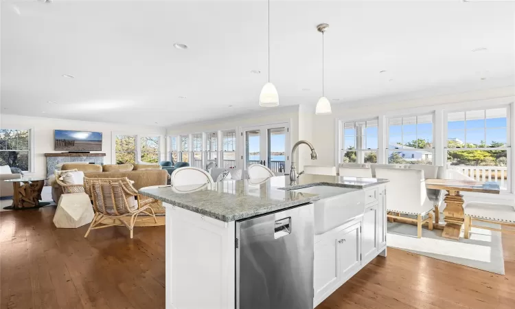 Kitchen with white cabinetry, stone counters, hanging light fixtures, stainless steel dishwasher, and a center island with sink