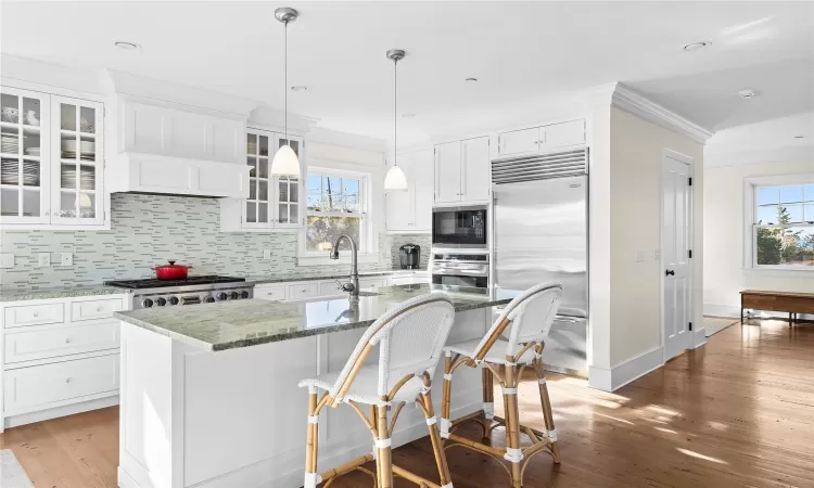 Kitchen featuring dark stone counters, a center island with sink, white cabinets, built in appliances, and plenty of natural light