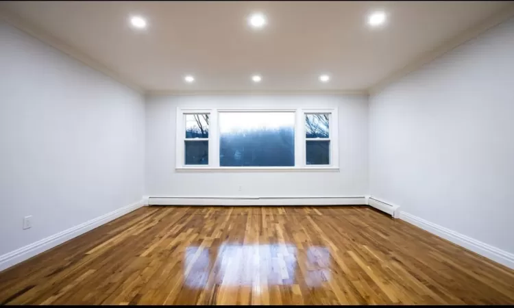 Spare room featuring hardwood / wood-style floors, crown molding, and a baseboard heating unit