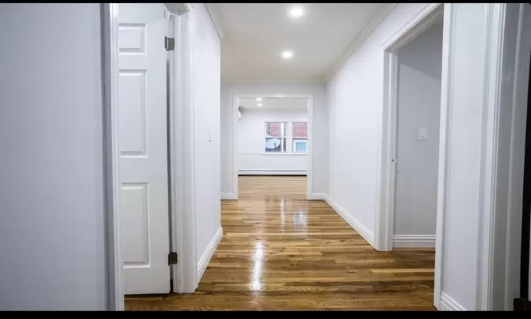 Hall with hardwood / wood-style floors, ornamental molding, and a baseboard heating unit