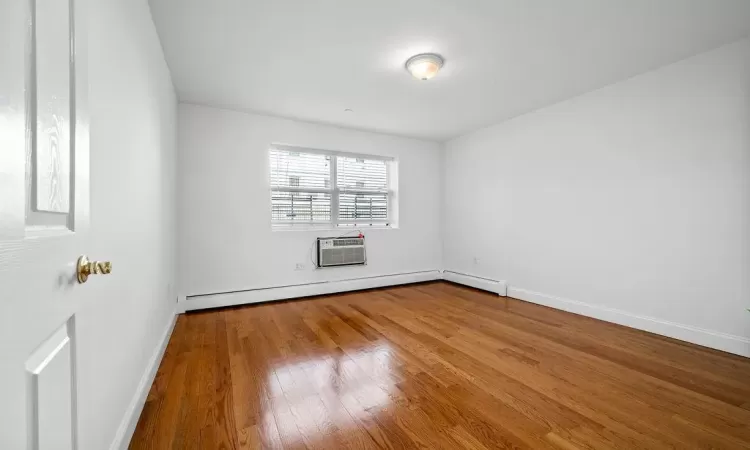 Empty room with wood-type flooring, baseboard heating, and a wall mounted AC