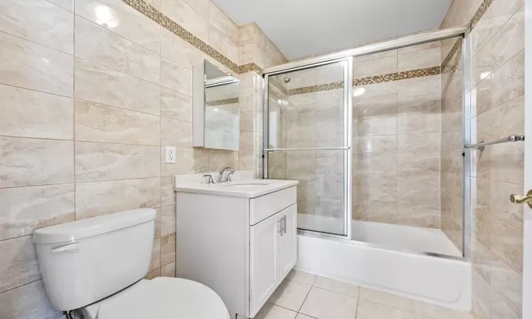 Full bathroom featuring vanity, tile patterned flooring, toilet, enclosed tub / shower combo, and tile walls