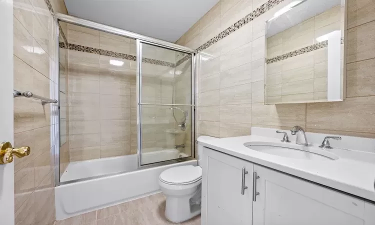 Full bathroom with bath / shower combo with glass door, vanity, tile walls, tile patterned flooring, and toilet