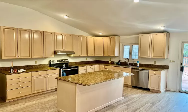 Kitchen featuring lofted ceiling, dark stone counters, sink, a kitchen island, and stainless steel appliances