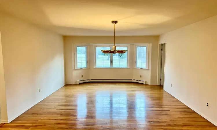 Spare room with light hardwood / wood-style flooring, baseboard heating, and a notable chandelier