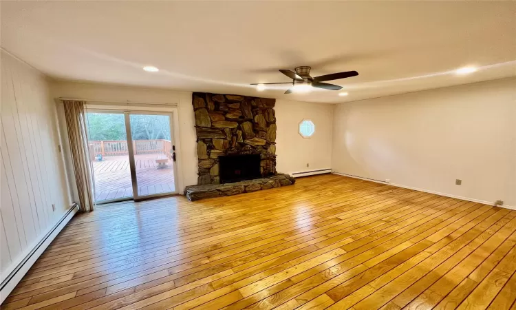 Unfurnished living room with light hardwood / wood-style flooring, a stone fireplace, ceiling fan, and a baseboard heating unit